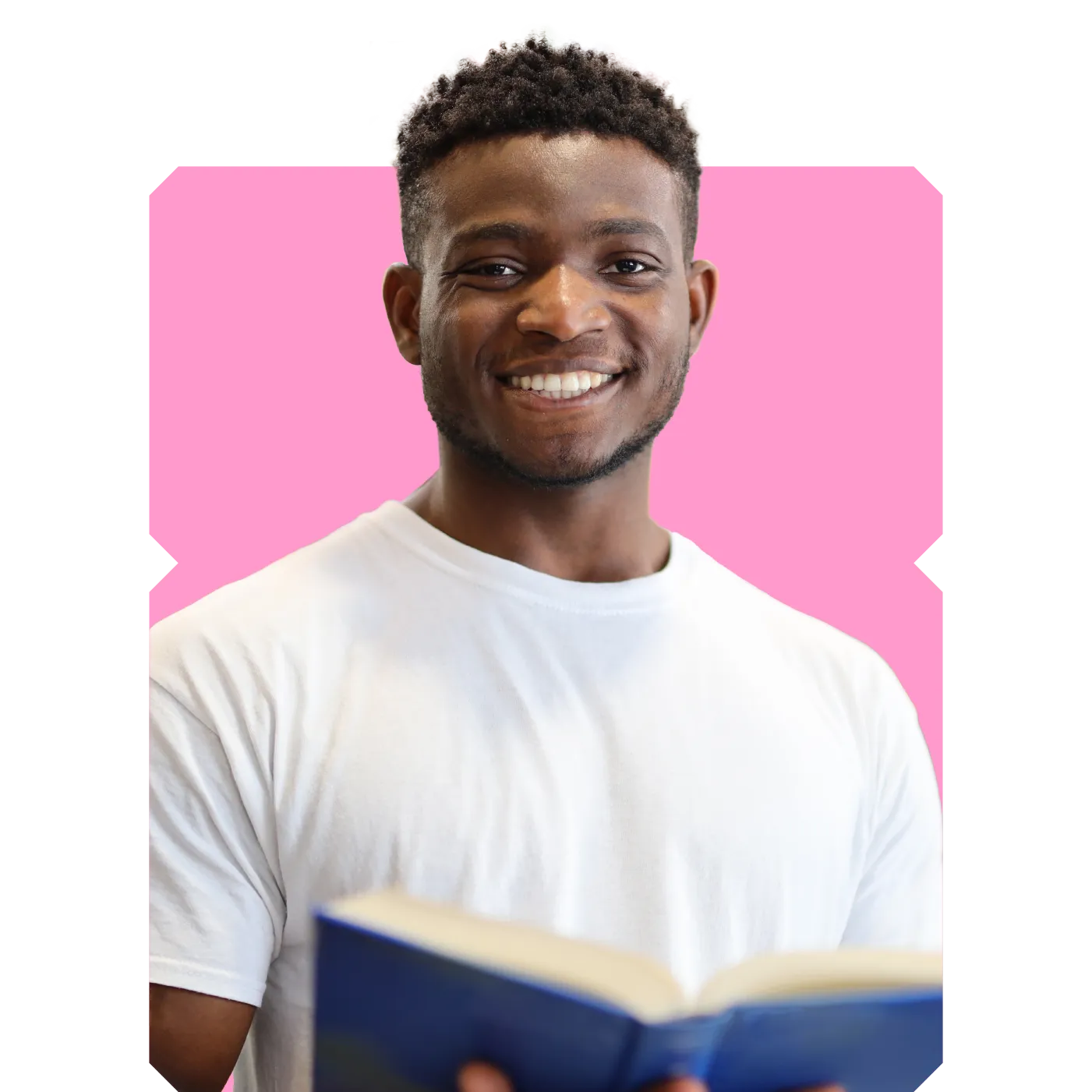 Smiling young man in a white T‑shirt holding an open book against a pink background