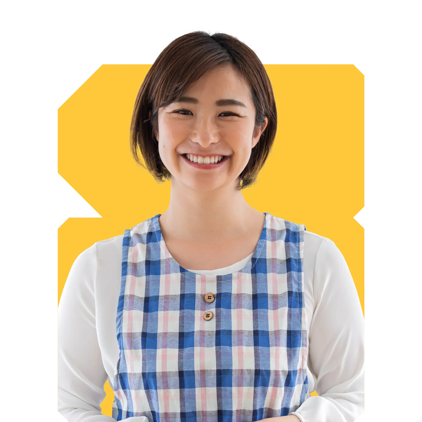 Smiling woman wearing a blue-and-pink checked pinafore over a white top against a yellow background