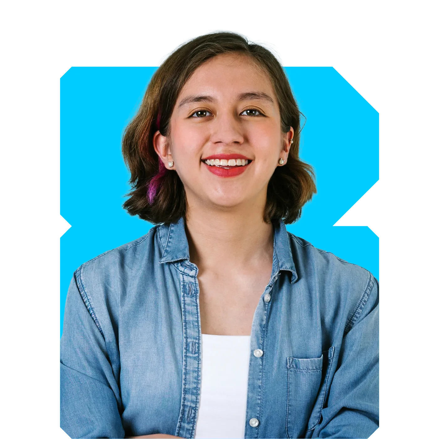 Smiling young woman with short brown hair and a purple streak, wearing a denim shirt against a bright blue background.