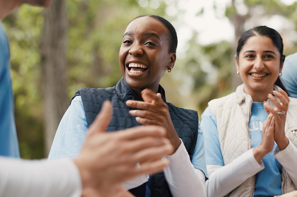 Two people in light-blue shirts smiling and applauding at an outdoor community event