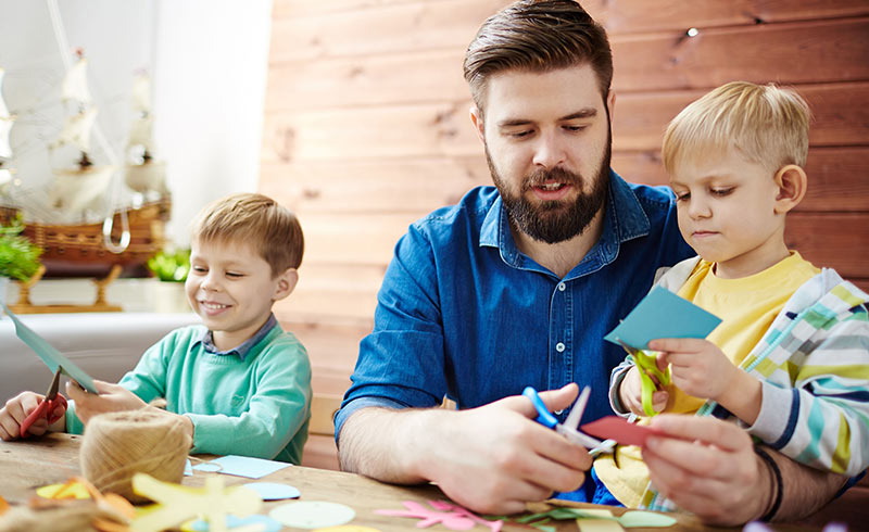 Man helping two young boys cut coloured paper to make craft shapes