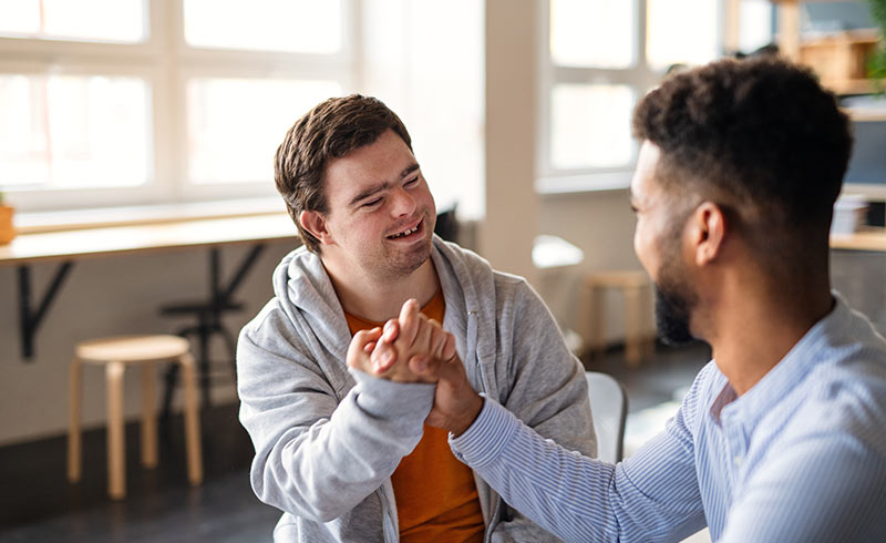 Two men smiling and clasping hands in a bright room, showing support and friendly connection