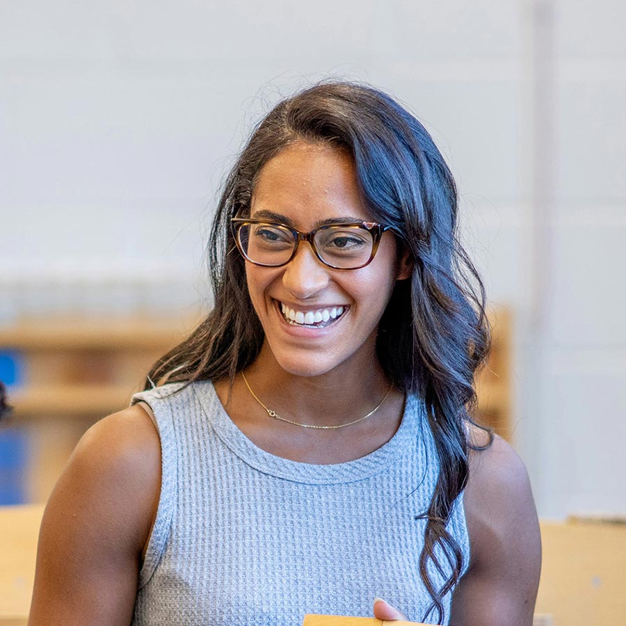 Smiling young woman with glasses and grey sleeveless top holding a yellow notebook