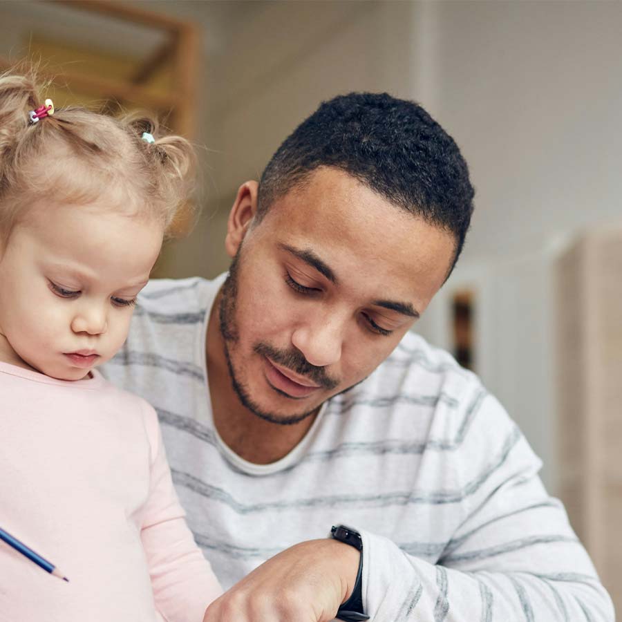 Man helping young child draw, pointing to paper as the child holds a pencil