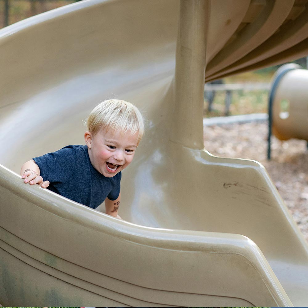 Toddler laughing as they come down a beige spiral playground slide
