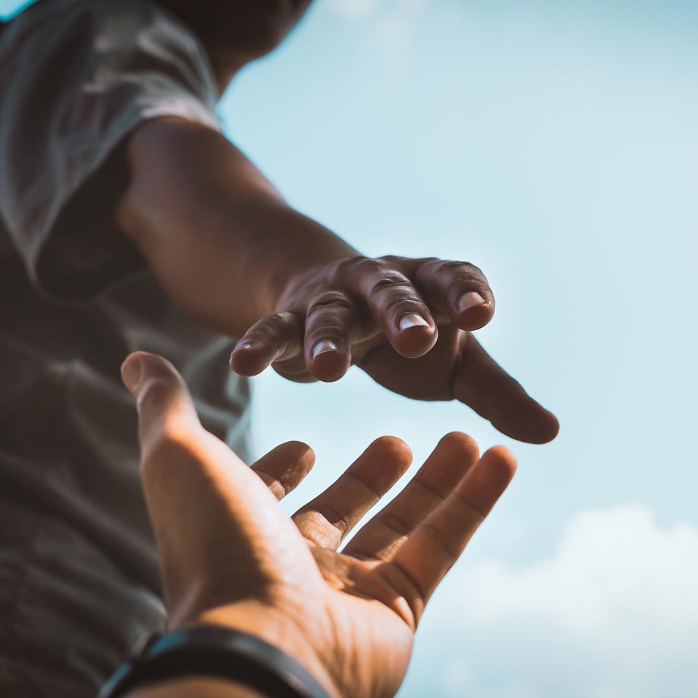 Two hands reaching toward each other against a blue sky, one offering support