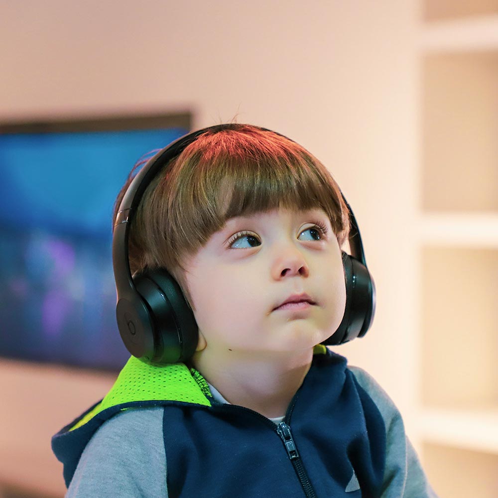 Child wearing black over-ear headphones, gazing upward with a thoughtful expression