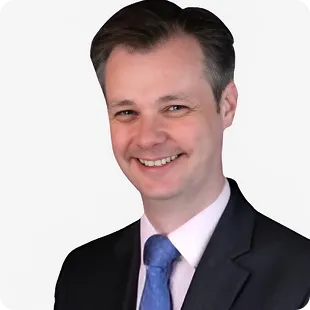 Smiling man in dark suit and blue tie on plain white background.