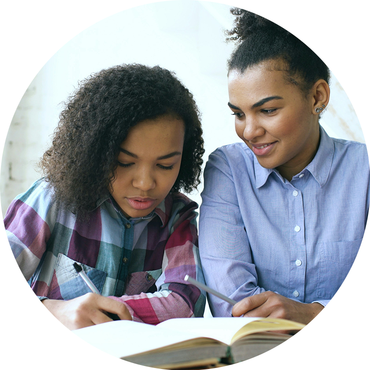 Young woman helping a girl with homework, both writing beside an open textbook