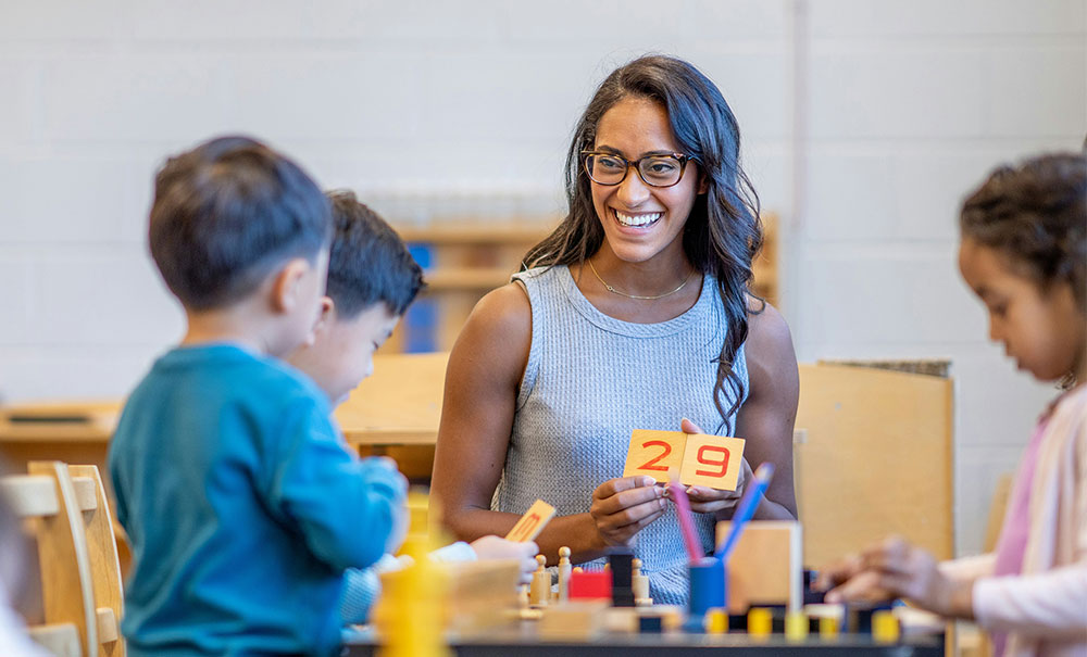 Early years teacher smiling, showing number cards '2' and '9' to young children during a counting activity
