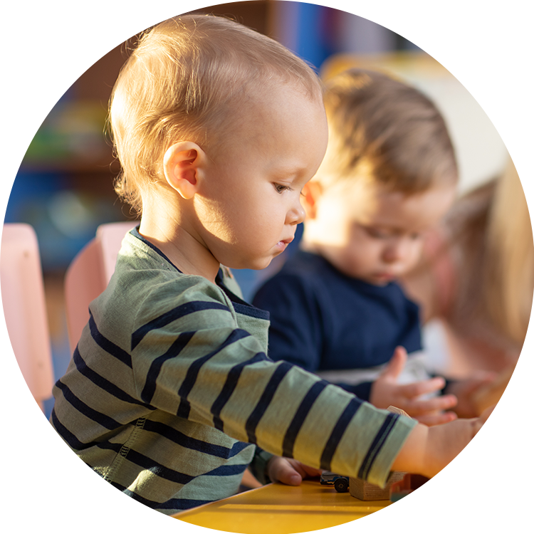 Toddler in a striped top and another child playing with toy cars at a daycare table